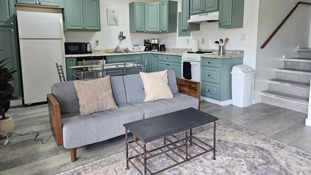 A modern kitchen with teal cabinets, a grey sofa, and a wooden coffee table. - Apartment Close to Hospital and UAA (Anchorage)