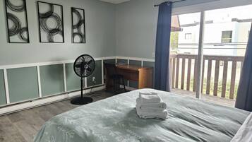 A bedroom with a bed, a desk, a chair, and a fan. There are three wall art pieces above the bed.