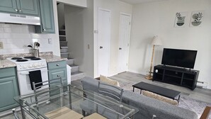 A modern kitchen with a dining area, a grey sofa, a TV, and a staircase. - Apartment Close to Hospital and UAA (Anchorage)