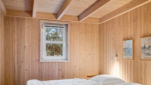 A wooden-paneled bedroom with a bed, a window, and two framed pictures on the wall.