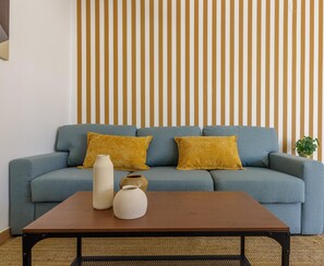 Una sala de estar con un sofá, dos almohadas color mostaza, una mesa de centro de madera y un jarrón.