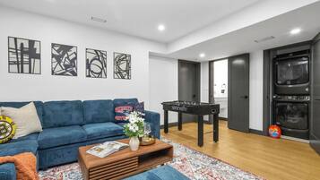 A modern living room with a blue sofa, a foosball table, and abstract wall art.