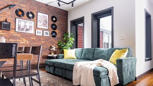 A cozy living room with a green sofa, a coffee table, and a brick wall adorned with vinyl records and framed photos.