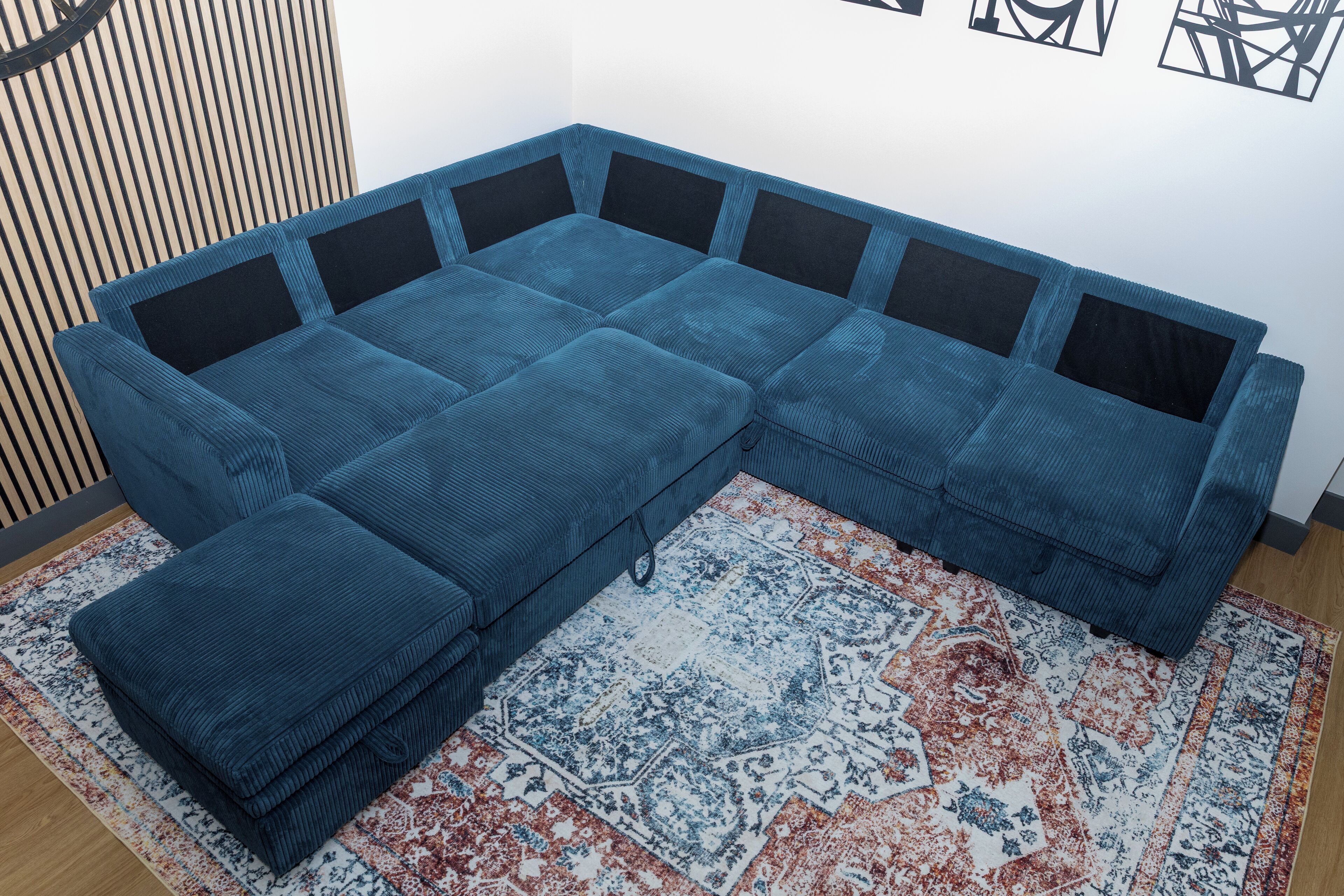 Un sofá modular con un reposapiés a juego, una alfombra estampada y un panel de pared de listones de madera.