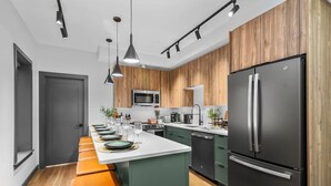 A modern kitchen with a central island, stainless steel appliances, and wooden cabinetry. - Loft Condo Free Parking/MIT/Harvard/TD Garden (Somerville)