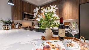 A modern kitchen with wooden cabinets, a white countertop, a vase with white flowers, a wine bottle, and a wine glass.