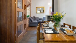 Un coin repas chaleureux avec une table en bois dressée pour deux personnes, un canapé en arrière-plan et un miroir au mur.