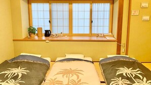 A hotel room with two beds, a window with curtains, a small table with a plant and a kettle, and a wall-mounted air conditioner. - ALOHADAYS Nishijin Guesthouse (Kyoto)