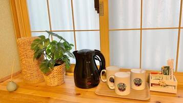 A wooden table with a black coffee pot, four mugs, a woven basket, and a potted plant.