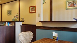 A restaurant interior with a wooden table, wicker chair, and wall art. - ALOHADAYS Nishijin Guesthouse (Kyoto)