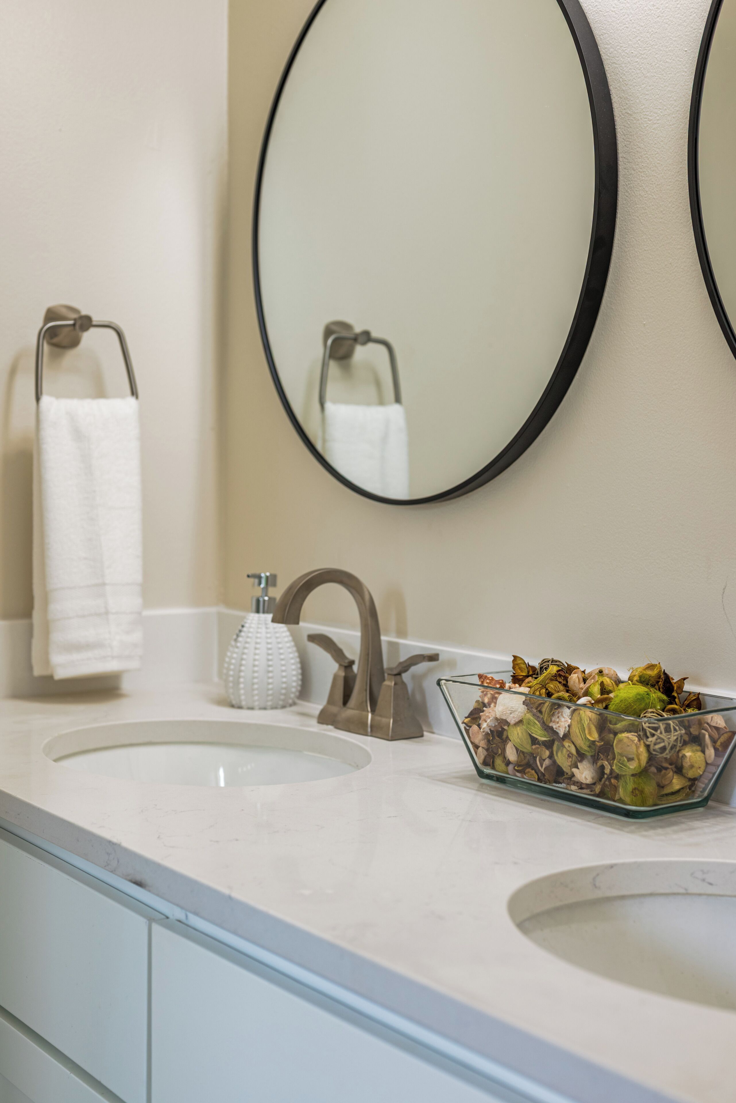 Un baño con un lavabo blanco, un espejo y un recipiente de vidrio con flores secas.