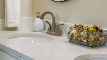 Un baño con un lavabo blanco, un espejo y un recipiente de vidrio con flores secas.