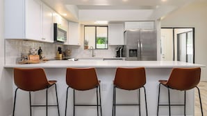 Eine moderne Küche mit weißen Schränken, einem Edelstahlkühlschrank und drei Barhocker.