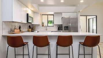 Una cocina moderna con armarios blancos, un refrigerador de acero inoxidable y tres taburetes de bar.