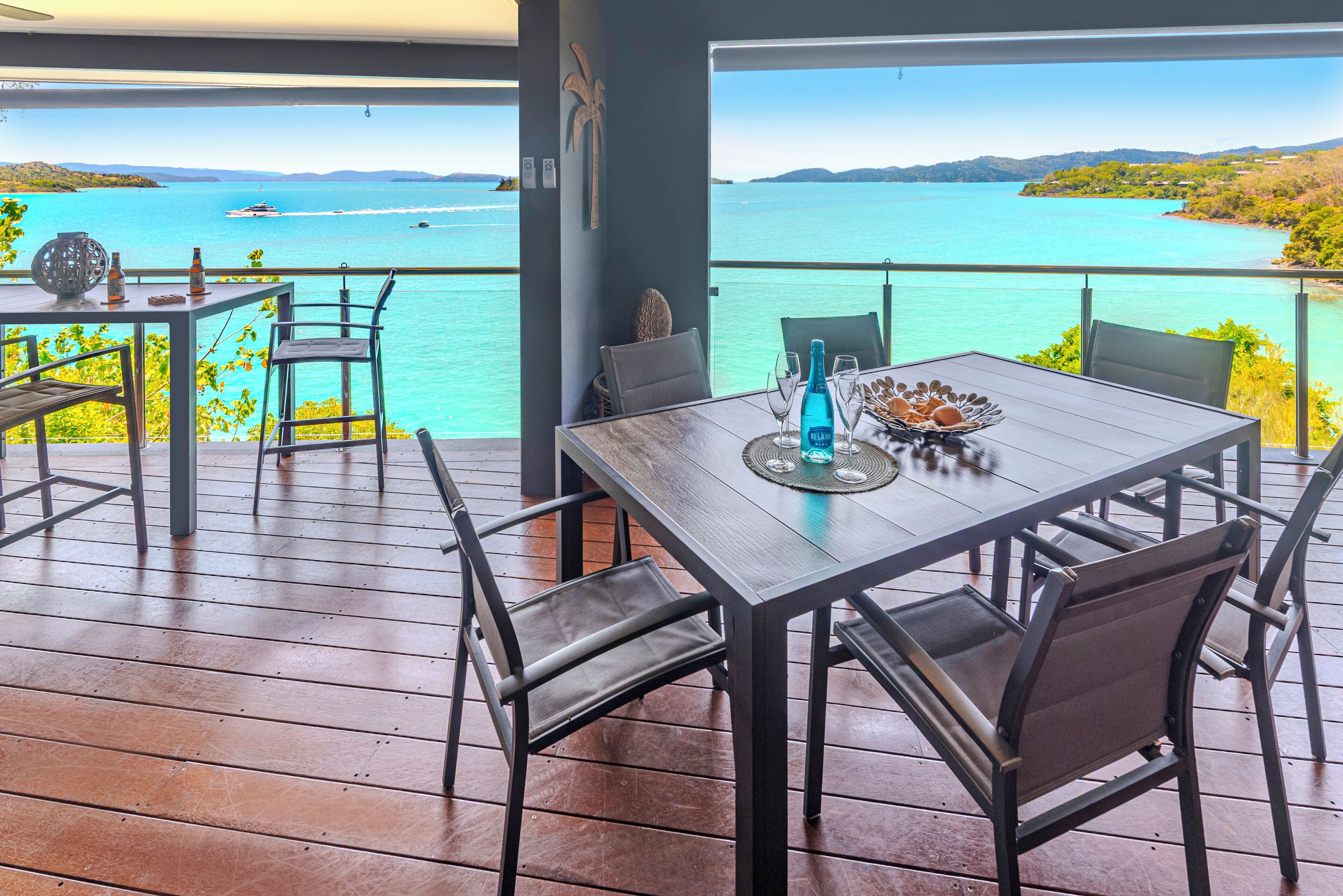 A wooden deck with a table and chairs overlooking a turquoise sea.