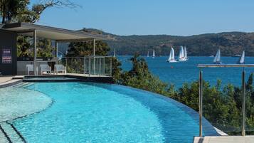 A swimming pool with a view of sailboats on the water, surrounded by greenery and hills.