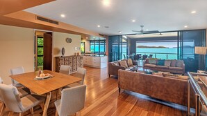 Un área de estar moderna con una mesa de comedor de madera, asientos cómodos, una cocina y un balcón con vista al mar.