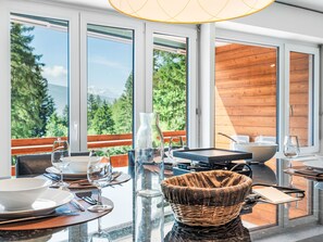 Uma sala de jantar com vista para uma floresta e montanhas, com uma mesa posta, pratos, copos e talheres.