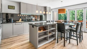 Une cuisine moderne dotée d’un îlot central, de luminaires suspendus et offrant une vue sur l’extérieur.