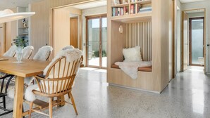 Een modern interieur met een houten eettafel, zachte witte stoelen, een ingebouwde boekenkast en een gezellige zithoek met een zachte witte plaid.