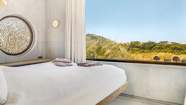 Een slaapkamer met een groot raam, een decoratieve ronde wandversiering en een bed met handdoeken.