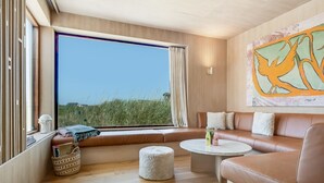 Een moderne woonkamer met een groot raam, een bruine leren bank, een ronde salontafel en een schilderij aan de muur.