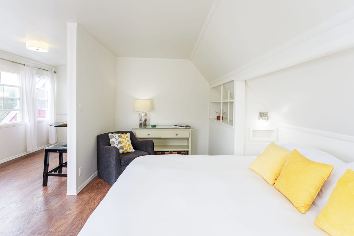 Een slaapkamer met een groot bed, een bureau, een stoel en een raam met gordijnen.