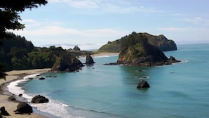 A coastal landscape with a sandy beach, clear turquoise waters, and rocky outcrops.