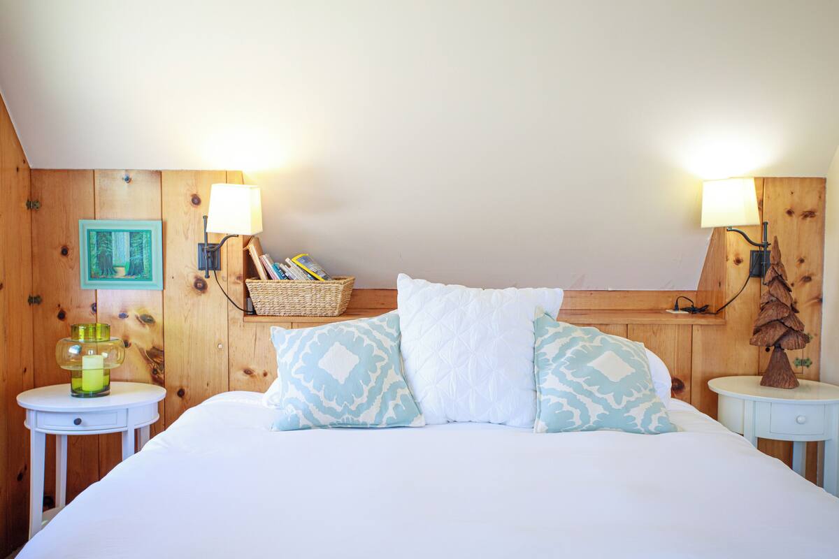 Een verzorgde slaapkamer met een groot bed, twee nachtkastjes, een lamp, een lijst met een afbeelding en een mand.