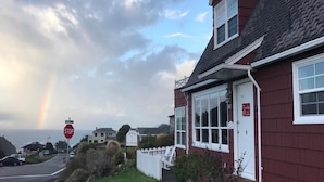 A red house with a white door and windows, a stop sign, and a rainbow in the background.
