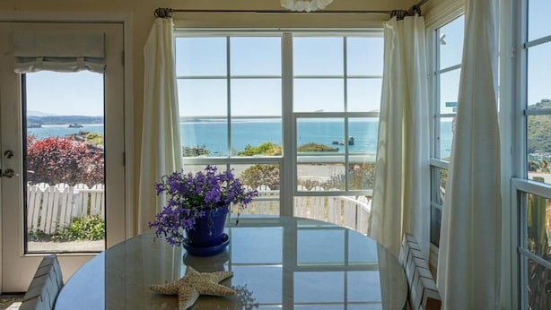 A room with a large window offering a view of the sea and a white picket fence.