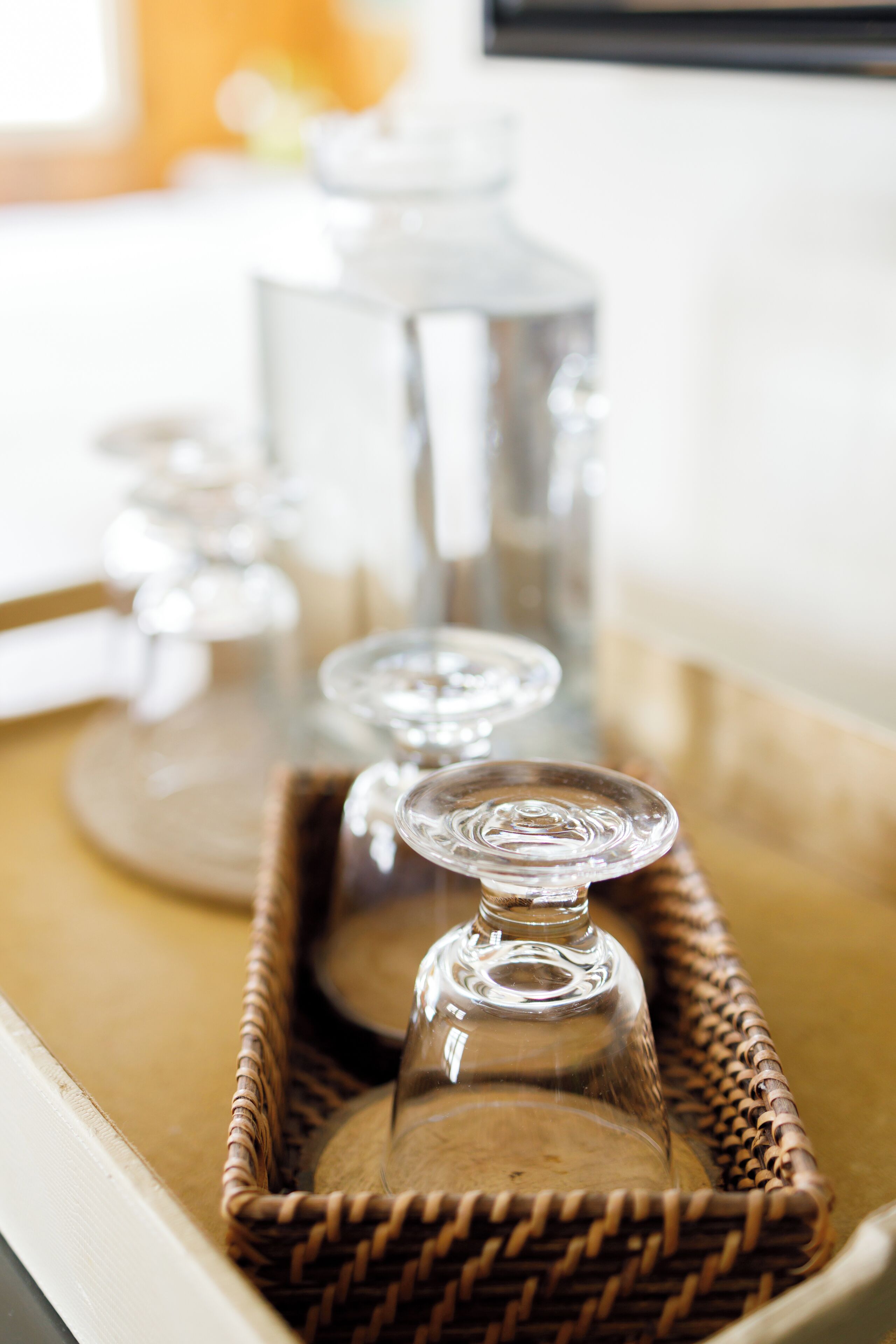 A wicker tray with glass bottles and a glass carafe on a table.