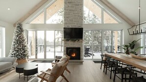 A spacious living area with a large fireplace, a dining table, and a cozy seating arrangement. - Spa • Sauna  • Salle de jeux • Terrasse • Foyer (Les Laurentides Regional County Municipality)