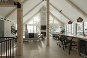 A spacious kitchen with a high ceiling, a fireplace, and a dining area with a long table and chairs.