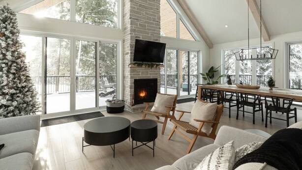 A spacious living room with a fireplace, large windows, and a high ceiling. - Spa • Sauna  • Salle de jeux • Terrasse • Foyer (Les Laurentides Regional County Municipality)