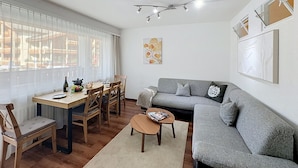 A modern living room with a grey sofa, wooden dining table, and chairs.