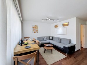 Una sala de estar moderna con comedor, un sofá gris, una mesa de comedor de madera y una pequeña mesa auxiliar.