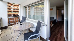 A balcony with a table and chairs, a bottle of wine, and a view of a wooden building.