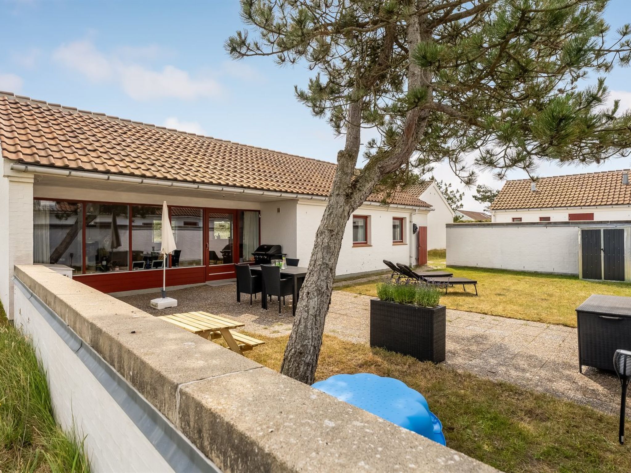 A modern house with a tiled roof, a patio with outdoor furniture, and a barbecue area.