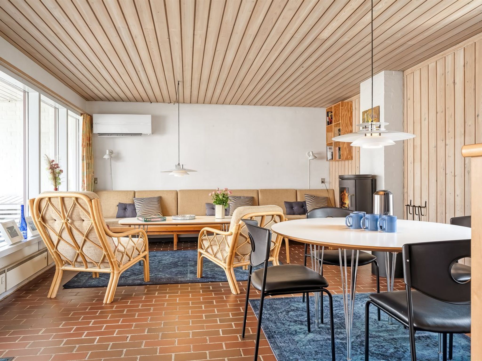 Un salon moderne avec un sol en briques, un plafond en bois et une table à manger ronde entourée de chaises.