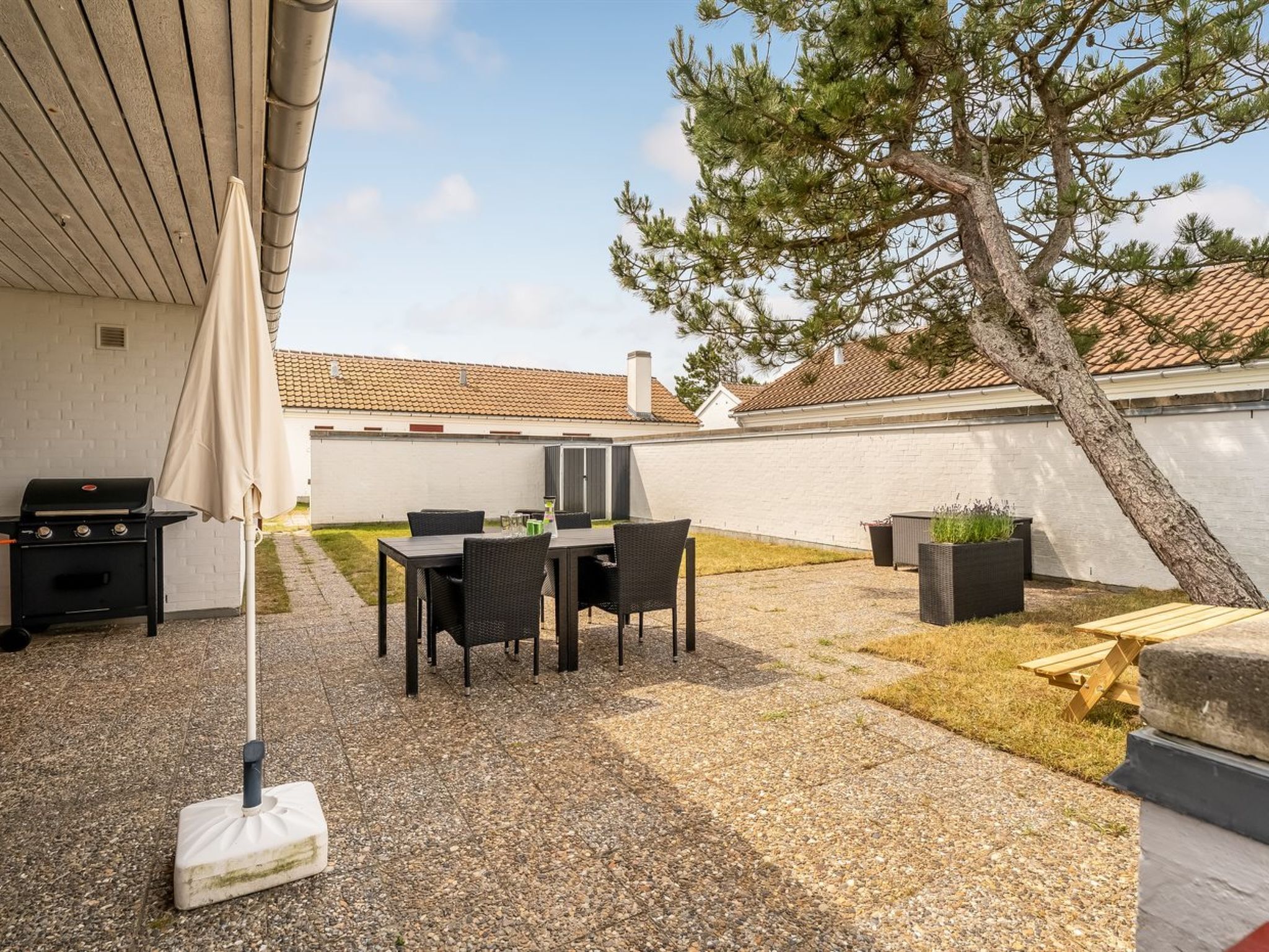 A patio with a grill, dining table, chairs, and a tree.