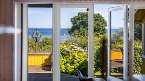 A view from a room with large sliding glass doors to a deck, overlooking a body of water and a garden with colorful flowers. - "Ephra" - 150m from the sea by Interhome (Bjert)