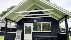A small, dark wooden structure with a white door and window, a picnic table, and a white grill on the side. - 4 Person Holiday Park Home in Malling (Malling)