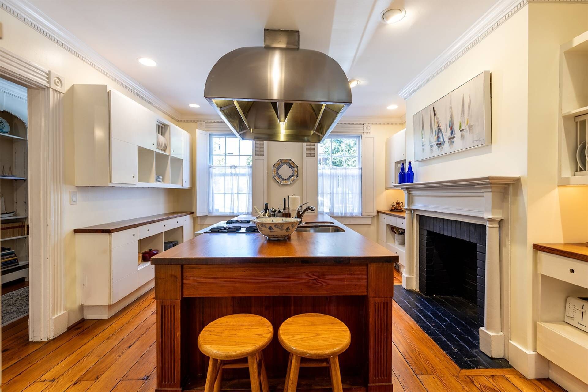 Una cocina amplia con una isla central, taburetes de madera, una chimenea y un ventanal grande.