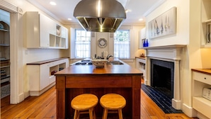 Una cocina amplia con una isla central, taburetes de madera, una chimenea y un ventanal grande.