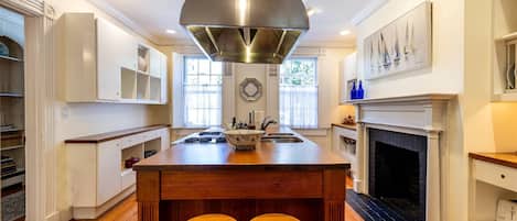 Una cocina amplia con una isla central, taburetes de madera, una chimenea y un ventanal grande.