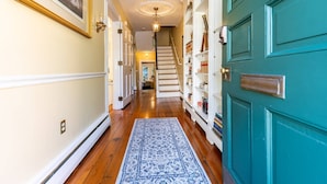 Un pasillo con piso de madera, un tapete azul estampado, una escalera y una puerta color turquesa con una estantería.