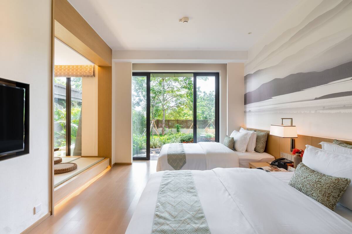 A modern hotel room with two beds, a large window, and a flat-screen TV.