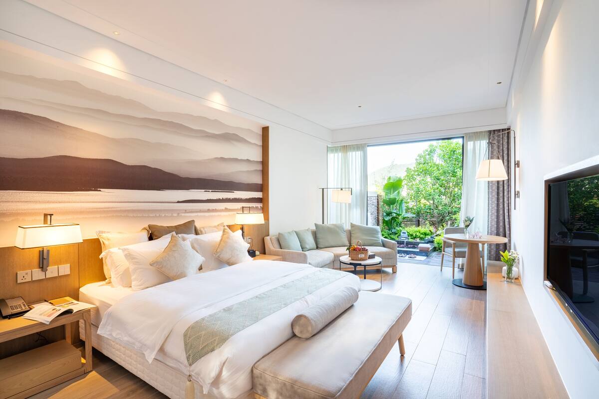 A modern hotel room with a large bed, a sofa, a small table, and a TV.