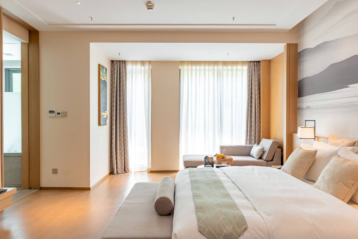 A hotel room with a large bed, a sofa, a desk, and a view of the sea through the windows.